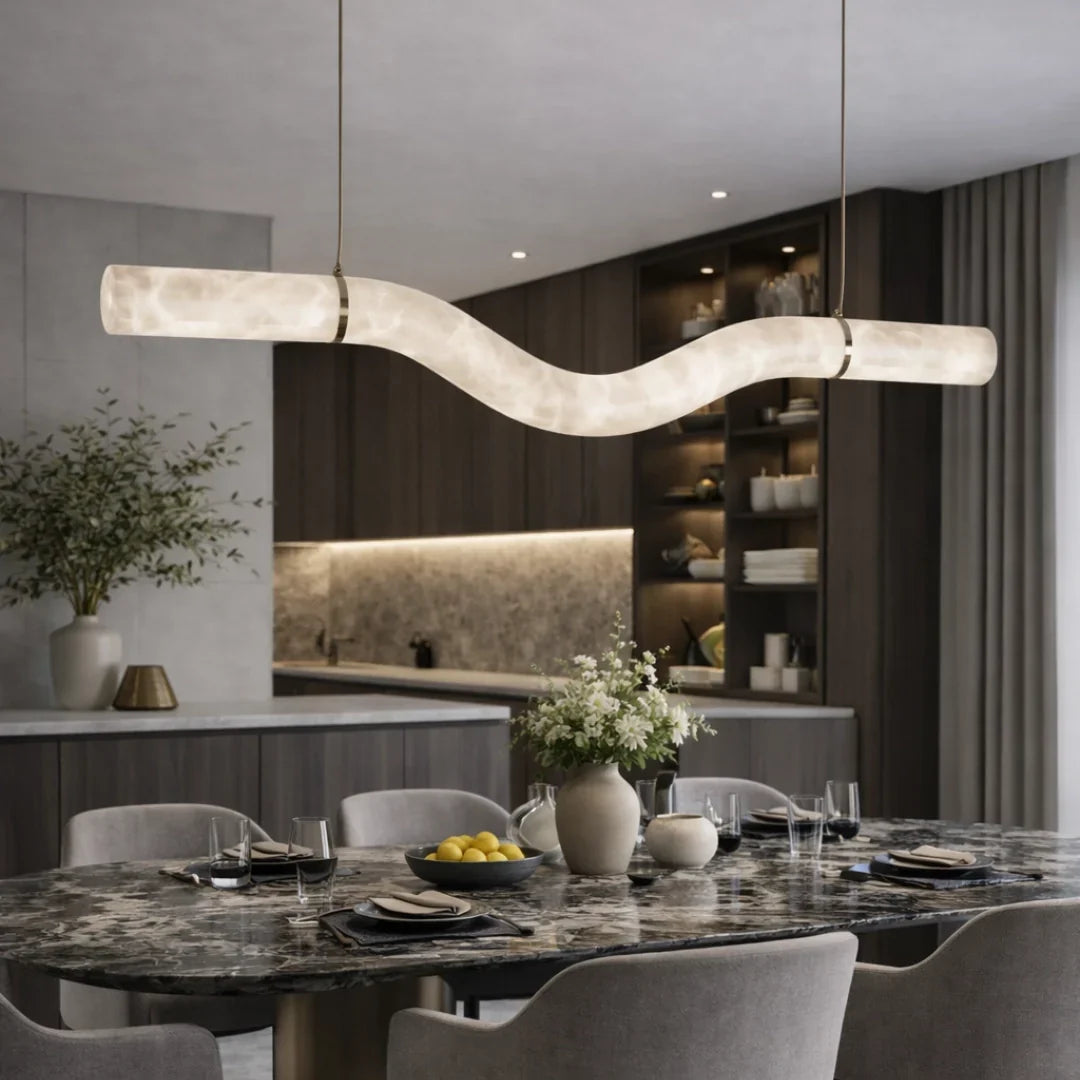 Illuminated W-Curve alabaster pendant above a dark dining table with kitchen cabinetry behind it